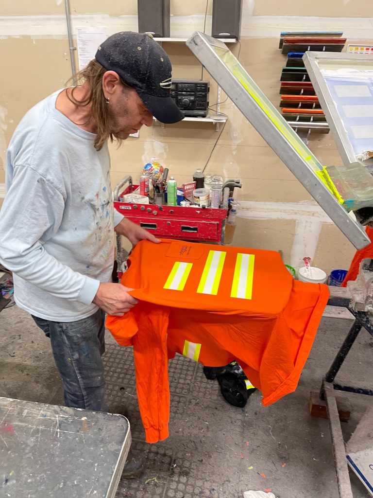 Ed screen prints safety stripes onto an orange shirt